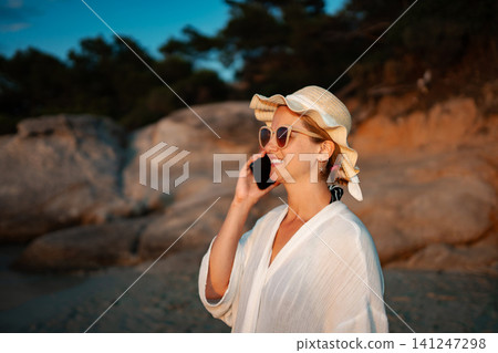 Woman talking on smartphone enjoying sunset beach vacation Woman talking on smartphone enjoying sunset beach vacation 141247298