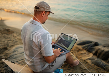 Adult male working remote on beach with laptop Adult male working remote on beach with laptop 141247382