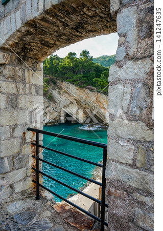 Stone Wall View of Turquoise Sea with Boat and Rocky Cave Coast 141247635
