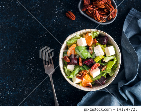 Healthy winter salad with beet cubes, feta cheese, orange segments and pecans in bowl. Flat lay on dark textured background with copy space. Perfect for restaurant menu or organic diet blog. Top view Healthy winter salad with beet cubes, feta cheese, orange segments and pecans in bowl. Flat lay on dark textured background with copy space. Perfect for restaurant menu or organic diet blog. Top view 141247723