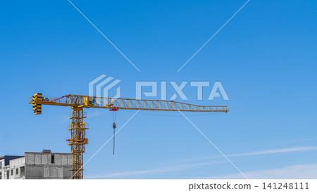 Photo of the construction of multi-storey building with a monolithic frame and walls erected with masonry from cellular foam blocks using an orange tower crane against blue background sky. Copy space Photo of the construction of multi-storey building with a monolithic frame and walls erected with masonry from cellular foam blocks using an orange tower crane against blue background sky. Copy space 141248111