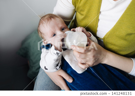 Close-up of mother bottle-feeding her cute infant baby at home. Close-up of mother bottle-feeding her cute infant baby at home. 141248131