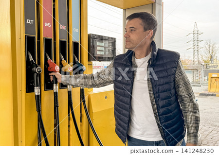 Man selecting fuel pump at gas station with yellow dispenser and multiple octane options Man selecting fuel pump at gas station with yellow dispenser and multiple octane options 141248230