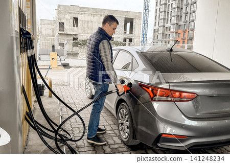 Man refueling silver sedan at gas station with construction site background Man refueling silver sedan at gas station with construction site background 141248234