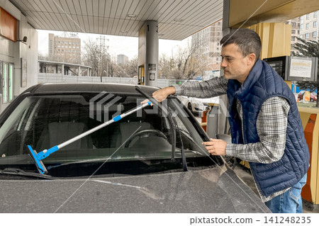 Man cleaning car windshield at gas station with squeegee tool Man cleaning car windshield at gas station with squeegee tool 141248235