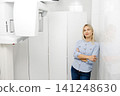 Dentist posing in her office next to a dental x-ray machine 141248630
