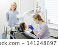 Dentist wearing mask and gloves examining young boy in dental clinic 141248697