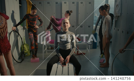 Overwhelmed Female Athlete Closing Eyes with Smartphone inside Dressing Room Overwhelmed Female Athlete Closing Eyes with Smartphone inside Dressing Room 141248756