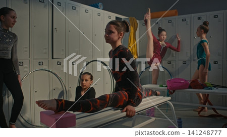 Flexible Girl in Black and Red Gymnastics Leotard Performs Deep Over Split on Wooden Bench 141248777
