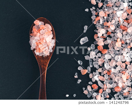 Coarse pink himalayan salt crystals in a dark wooden spoon and scattered on black slate stone background. Top view flat lay composition with copy space. Perfect for cooking, spa or wellness concept 141248796