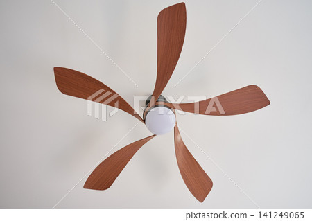 Ceiling fan with five wooden blades and integrated light mounted on white ceiling Ceiling fan with five wooden blades and integrated light mounted on white ceiling 141249065