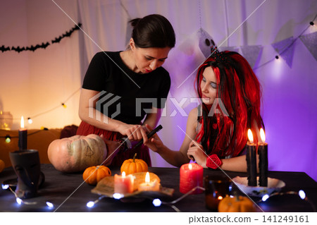 Mother With Little Daughter Prepares The Room For A Festive Halloween By Drawing A Pumpkin Face Mother With Little Daughter Prepares The Room For A Festive Halloween By Drawing A Pumpkin Face 141249161