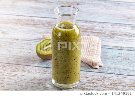 Green kiwi smoothie in glass carafe on rustic wooden table with halved fruit and cloth napkin Green kiwi smoothie in glass carafe on rustic wooden table with halved fruit and cloth napkin 141249191