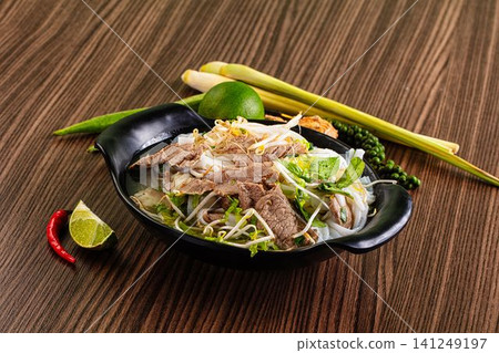 Pho bo bowl with beef slices bean sprouts and fresh herbs on wooden table Pho bo bowl with beef slices bean sprouts and fresh herbs on wooden table 141249197