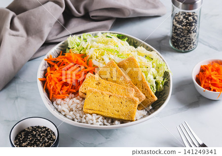 A small portion of rice with grilled tofu, Chinese cabbage and carrots in a bowl on the table 141249341