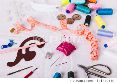 Sewing thread, measuring tape, pattern, and sewing accessories on the white fabric Sewing thread, measuring tape, pattern, and sewing accessories on the white fabric 141249350