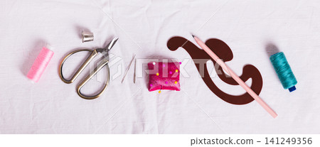 Scissors, measuring tape, pattern, thimble, thread and sewing accessories on white fabric top view web banner 141249356