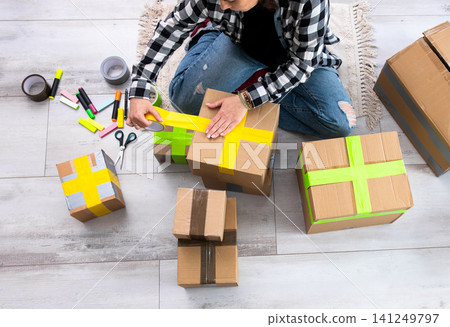 Girl Packing Cardboard Boxes And Sealing Them With Colorful Tapes Girl Packing Cardboard Boxes And Sealing Them With Colorful Tapes 141249797