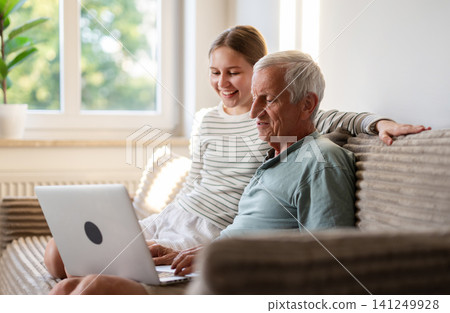 Little Girl And Grandfather Having Fun Watching Videos Together At Home On A Laptop Little Girl And Grandfather Having Fun Watching Videos Together At Home On A Laptop 141249928