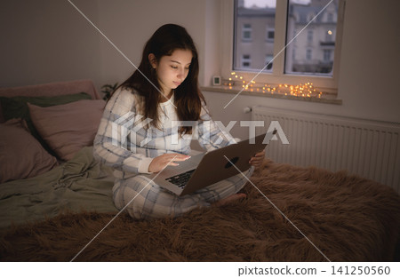 Girl sits on bed and uses laptop to chatting with friends in social media Girl sits on bed and uses laptop to chatting with friends in social media 141250560