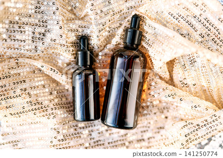 Skincare serum dropper bottles on sparkling golden fabric Skincare serum dropper bottles on sparkling golden fabric 141250774