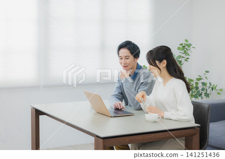 A couple watching a computer in the dining room A couple watching a computer in the dining room 141251436