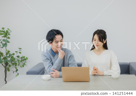 A couple watching a computer in the dining room A couple watching a computer in the dining room 141251444