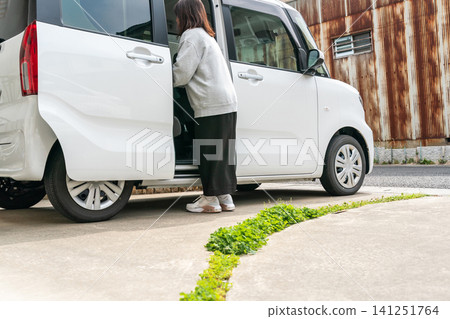 一位家庭主婦從一輛側滑門敞開的輕型汽車裡卸下行李。 一位家庭主婦從一輛側滑門敞開的輕型汽車裡卸下行李。 141251764
