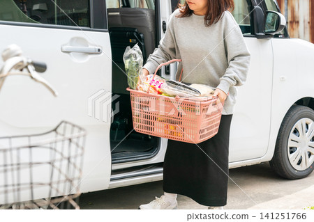 一位女士從超市回來後，提著購物籃從小型汽車走出來。 141251766