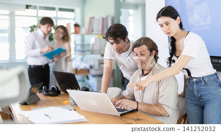 Group of coworkers gathered at one laptop and discuss working issues 141252032
