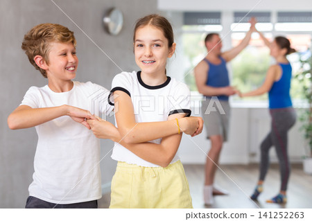 Happy sister and brother and their mom and dad practicing modern teen dance with crossed hands while training together in wellness center Happy sister and brother and their mom and dad practicing modern teen dance with crossed hands while training together in wellness center 141252263