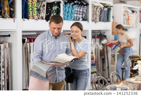 Adult man with wife choosing fabric upholstery in furniture salon Adult man with wife choosing fabric upholstery in furniture salon 141252336