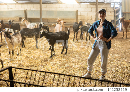 Positive woman employee standing with pitchforks in goat farmhouse padded with straw in autumn Positive woman employee standing with pitchforks in goat farmhouse padded with straw in autumn 141252339