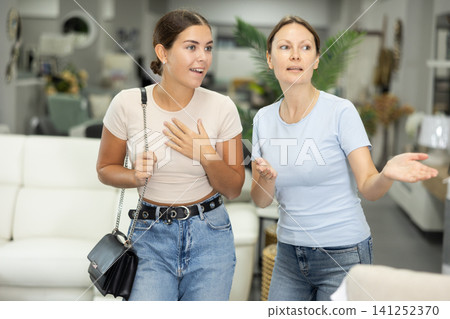 Two sister friends choose a sofa or bed in furniture store Two sister friends choose a sofa or bed in furniture store 141252370