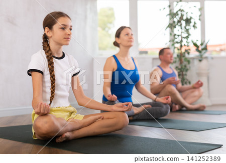 Pleasant preteen girl practicing lotus pose of yoga with her family Pleasant preteen girl practicing lotus pose of yoga with her family 141252389