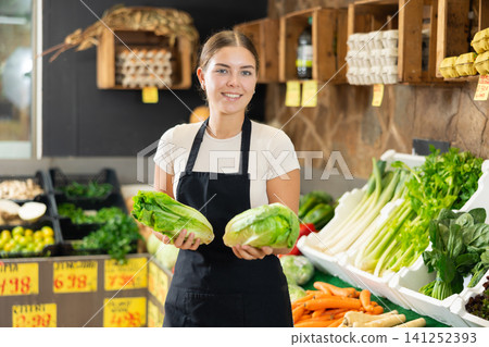 Girl employee was distracted for minute and stands smiling with china cabbage in hands. Girl employee was distracted for minute and stands smiling with china cabbage in hands. 141252393