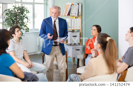 Youth girls and guys sit at circle, listen to senior man coach. Youth girls and guys sit at circle, listen to senior man coach. 141252474