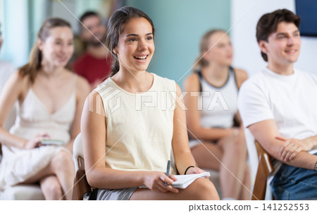 At meeting room during lecture, girl with classmates listen and laughing At meeting room during lecture, girl with classmates listen and laughing 141252553