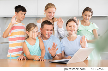 Large family is sitting in kitchen next to laptop and making video call to grandparents Large family is sitting in kitchen next to laptop and making video call to grandparents 141252566