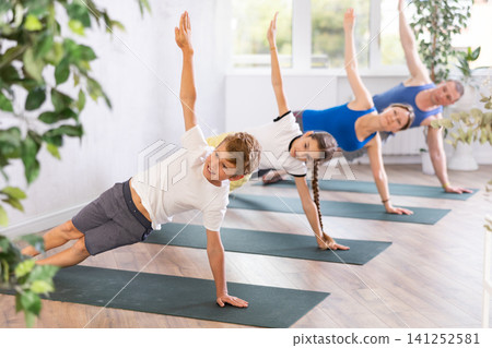 Kids and parents practicing Side Plank Pose or Vasisthasana on mats during family Hatha yoga class in studio Kids and parents practicing Side Plank Pose or Vasisthasana on mats during family Hatha yoga class in studio 141252581