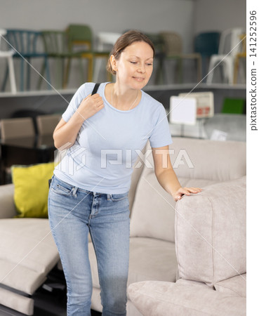 Woman in store inspects upholstered furniture. Woman in store inspects upholstered furniture. 141252596