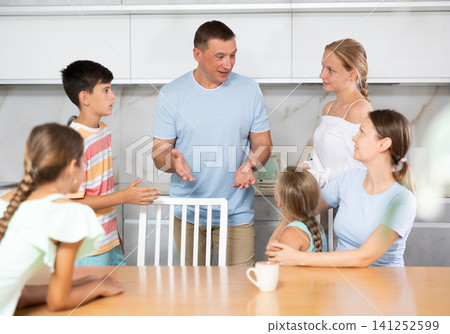 Friendly family gathered at table and cheerfully discuss past day. Friendly family gathered at table and cheerfully discuss past day. 141252599
