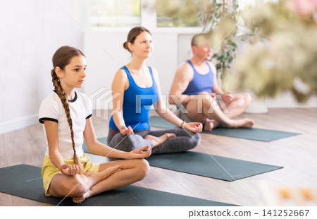 Pleasant preteen girl practicing lotus pose of yoga with her family Pleasant preteen girl practicing lotus pose of yoga with her family 141252667
