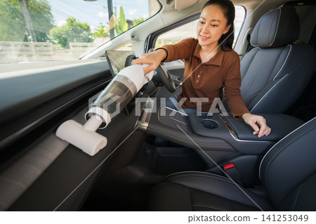woman using portable handheld vacuum cleaner to clean dust on an electric car dashboard woman using portable handheld vacuum cleaner to clean dust on an electric car dashboard 141253049