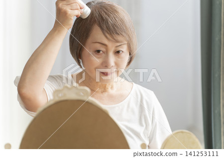 A senior woman styling her hair with a brush. A senior woman styling her hair with a brush. 141253111