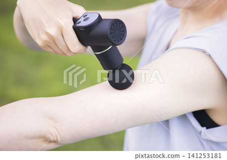 Young woman using a fascia release gun and massage gun outdoors Young woman using a fascia release gun and massage gun outdoors 141253181