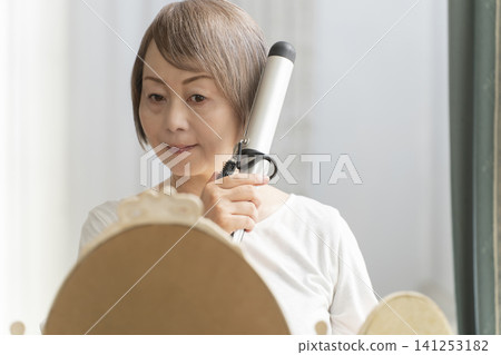 Senior woman styling her hair with a curling iron. Senior woman styling her hair with a curling iron. 141253182