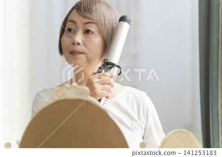 Senior woman styling her hair with a curling iron. Senior woman styling her hair with a curling iron. 141253183