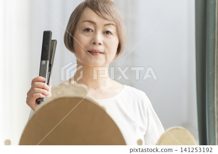 Senior woman styling her hair with a curling iron. 141253192