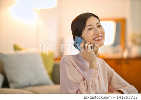 一位四十多歲的女性晚上在房間裡放鬆,看著她的智慧型手機。 一位四十多歲的女性晚上在房間裡放鬆,看著她的智慧型手機。 141253712